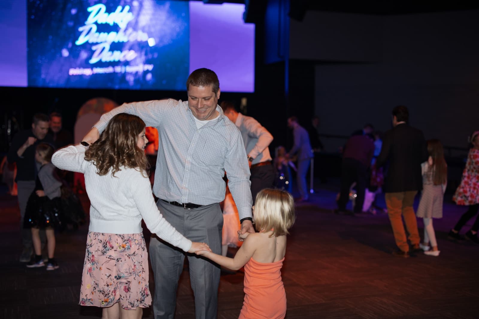 Father and daughters dancing at a church community event.