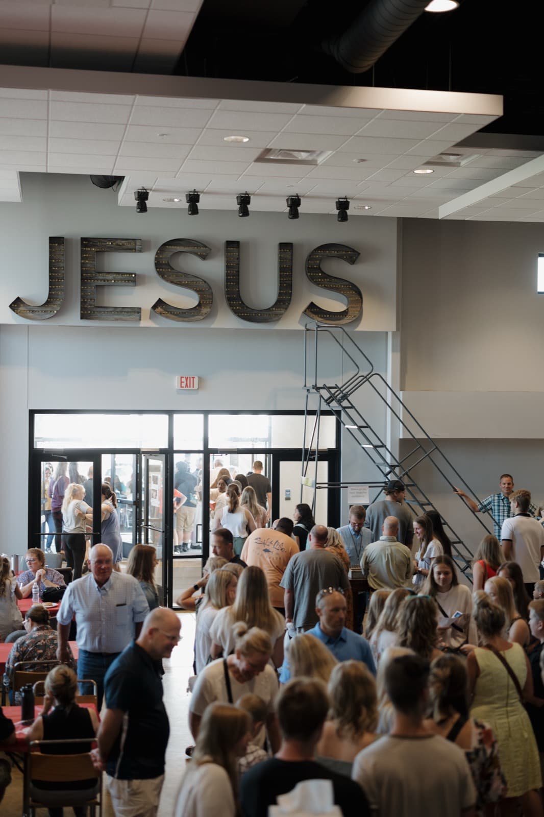 A full lobby on a Sunday morning beneath the large JESUS letters on the wall.