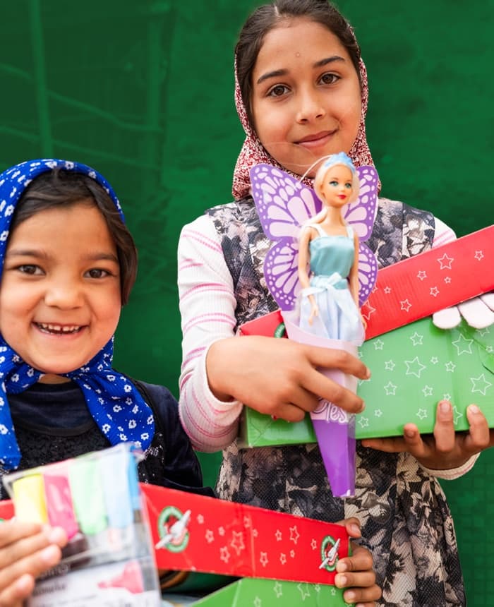 Two girls smiling as they hold the Operation Christmas Child shoebox gifts they received.